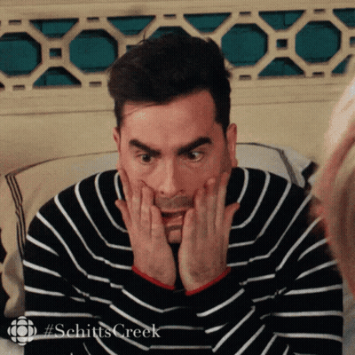 A Man In A Striped Sweater Is Making A Surprised Face With His Hands On His Face . GIF