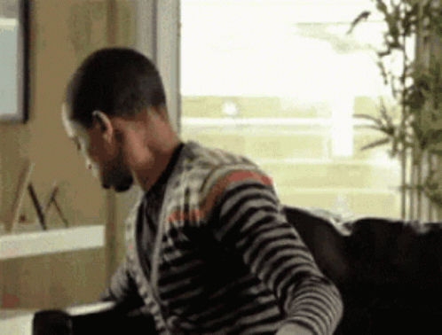 A Man In A Striped Sweater Is Sitting On A Couch In Front Of A Window . GIF