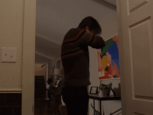 A Man In A Striped Sweater Is Standing In Front Of A Painting GIF