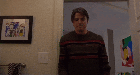 A Man In A Striped Sweater Stands In Front Of A Framed Picture On The Wall GIF