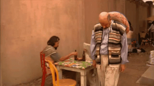A Man In A Striped Vest Is Standing Next To A Table GIF