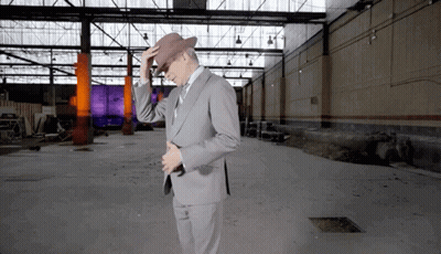 A Man In A Suit Adjusts His Hat In An Empty Building GIF