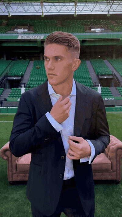 A Man In A Suit Adjusts His Tie In Front Of A Stadium That Says Dedicacao On It GIF