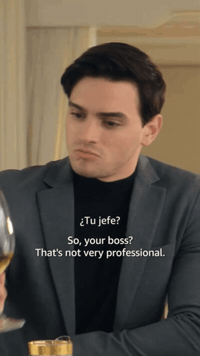 A Man In A Suit And A Black Turtleneck Is Talking To Another Man GIF