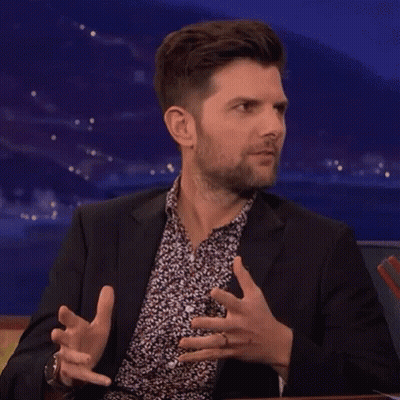 A Man In A Suit And A Floral Shirt Is Making A Funny Face While Sitting At A Table . GIF