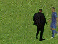 A Man In A Suit And A Man In A Blue Shirt Are Standing On A Green Field GIF