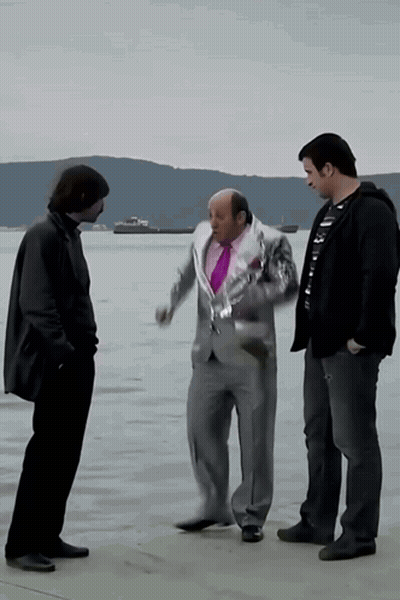 A Man In A Suit And A Purple Tie Talks To Two Other Men In Front Of A Body Of Water GIF