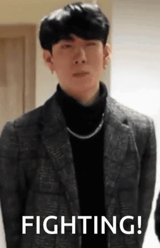 A Man In A Suit And A Turtleneck Is Standing In Front Of A Sign That Says Fighting ! GIF