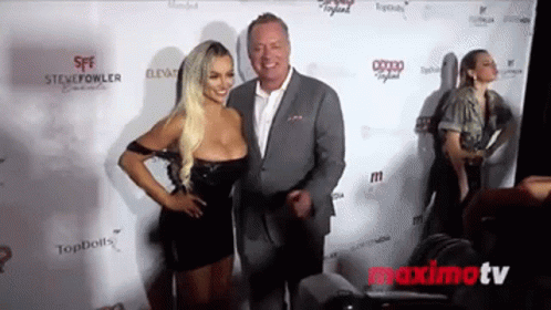 A Man In A Suit And A Woman In A Black Dress Pose For A Picture On A Red Carpet . GIF