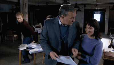 A Man In A Suit And A Woman In A Blue Sweater Are Standing In Front Of A Door That Says ' Exit ' GIF