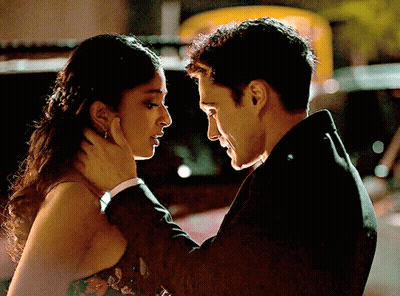 A Man In A Suit And A Woman In A Dress Are Looking At Each Other GIF