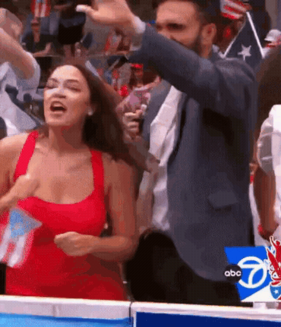 A Man In A Suit And A Woman In A Red Dress Are Standing Next To Each Other In A Crowd . GIF