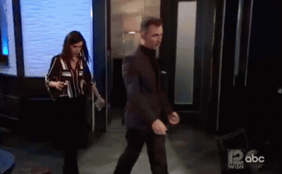 A Man In A Suit And A Woman In A Striped Shirt Are Walking Through A Doorway On Abc . GIF
