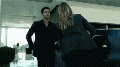 A Man In A Suit And A Woman In A Suit Are Standing Next To Each Other In Front Of A Car . GIF