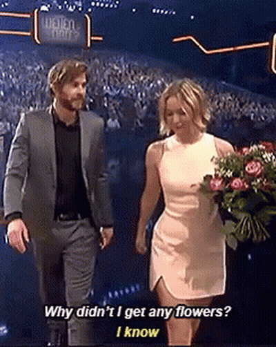A Man In A Suit And A Woman In A White Dress Holding A Bouquet Of Flowers Are Walking On A Stage . GIF