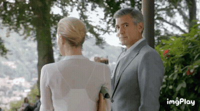 A Man In A Suit And A Woman In A White Shirt Are Looking At Each Other . GIF