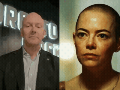 A Man In A Suit And A Woman With A Shaved Head In Front Of A Sign That Says Toronto GIF
