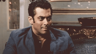 A Man In A Suit And Black Shirt Is Sitting On A Couch And Making A Funny Face . GIF
