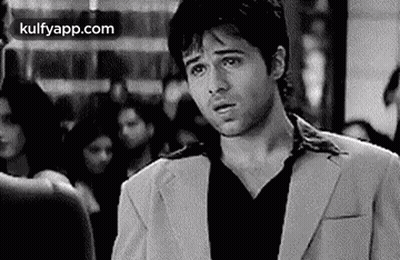 A Man In A Suit And Black Shirt Is Standing In A Crowded Room . GIF