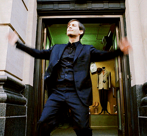 A Man In A Suit And Black Shirt Is Standing In A Doorway With His Arms Outstretched GIF