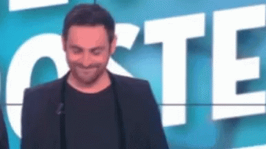 A Man In A Suit And Black Shirt Is Standing In Front Of A Sign That Says `` Cote '' . GIF