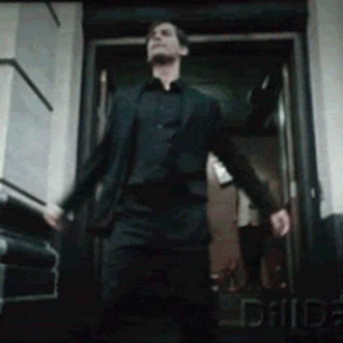 A Man In A Suit And Black Shirt Is Walking Out Of A Door GIF