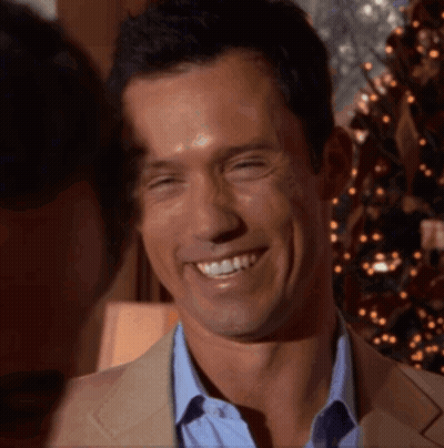 A Man In A Suit And Blue Shirt Smiles With A Christmas Tree In The Background GIF