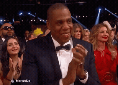 A Man In A Suit And Bow Tie Applauds In A Crowd Of People GIF