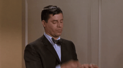 A Man In A Suit And Bow Tie Is Adjusting His Cuffs . GIF