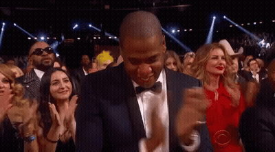 A Man In A Suit And Bow Tie Is Dancing In Front Of A Crowd Of People GIF