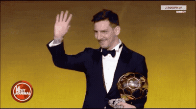A Man In A Suit And Bow Tie Is Holding A Soccer Ball And Waving . GIF