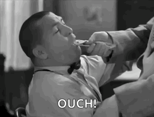 A Man In A Suit And Bow Tie Is Holding A Spoon In His Mouth And Says Ouch . GIF