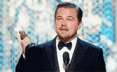 A Man In A Suit And Bow Tie Is Holding A Trophy While Standing In Front Of A Microphone . GIF