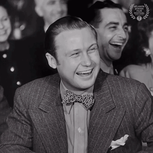 A Man In A Suit And Bow Tie Is Laughing With A Laurel Wreath That Says Atlanta International Film Festival On It GIF