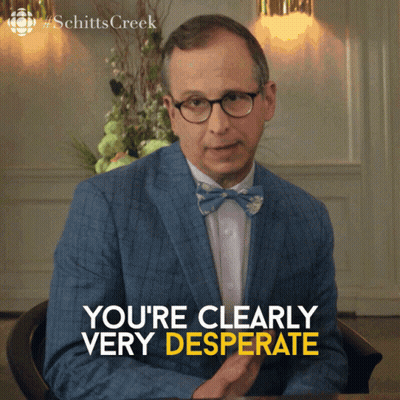 a man in a suit and bow tie is sitting at a table and says " you 're clearly very desperate "