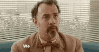 A Man In A Suit And Bow Tie Is Sitting In Front Of A Window With The Word We Written On It . GIF