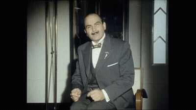 A Man In A Suit And Bow Tie Is Sitting On A Chair GIF