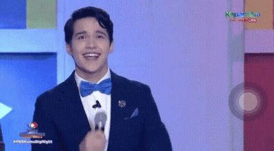 A Man In A Suit And Bow Tie Is Smiling While Standing In Front Of A Microphone . GIF
