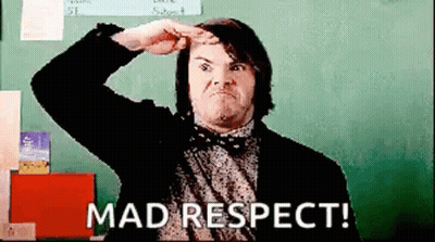 A Man In A Suit And Bow Tie Is Standing In Front Of A Blackboard And Making A Funny Face . GIF
