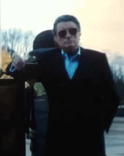 A Man In A Suit And Bow Tie Is Standing In Front Of A Building GIF