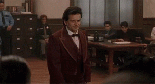A Man In A Suit And Bow Tie Is Standing In Front Of A Courtroom . GIF