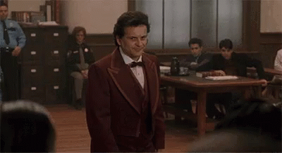 A Man In A Suit And Bow Tie Is Standing In Front Of A Courtroom . GIF