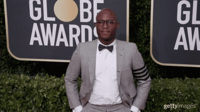 A Man In A Suit And Bow Tie Is Standing In Front Of A Sign That Says Globe Awards GIF