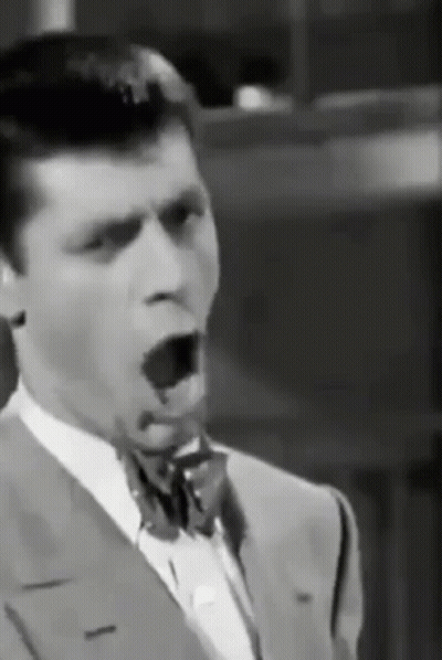 A Man In A Suit And Bow Tie Is Yawning . GIF