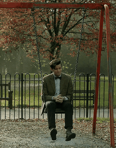 A Man In A Suit And Bow Tie Sits On A Swing In A Park GIF