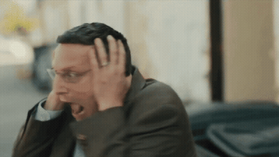 A Man In A Suit And Glasses Is Holding His Head GIF