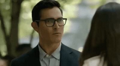 A Man In A Suit And Glasses Is Looking At A Woman In A White Shirt . GIF