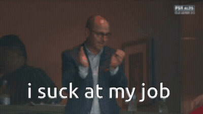 A Man In A Suit And Glasses Is Looking At His Phone With The Words I Suck At My Job Behind Him GIF