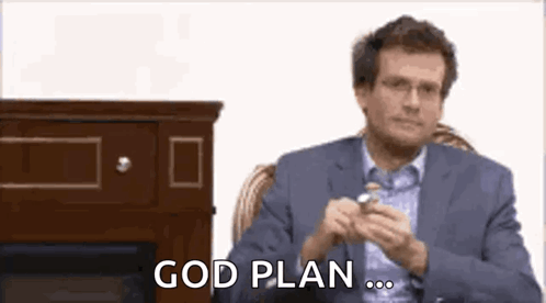 A Man In A Suit And Glasses Is Sitting In A Chair And Holding A Watch . GIF