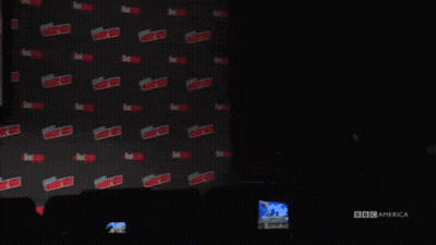 A Man In A Suit And Glasses Is Standing In Front Of A Wall With The Word Expo On It . GIF